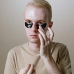 Un jeune homme applique des patchs sous les yeux pour une routine de soin rafraîchissante en intérieur.