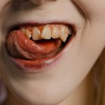 Détail d'un plan rapproché sur une bouche avec des crocs visibles et la langue, évoquant une esthétique de vampire.