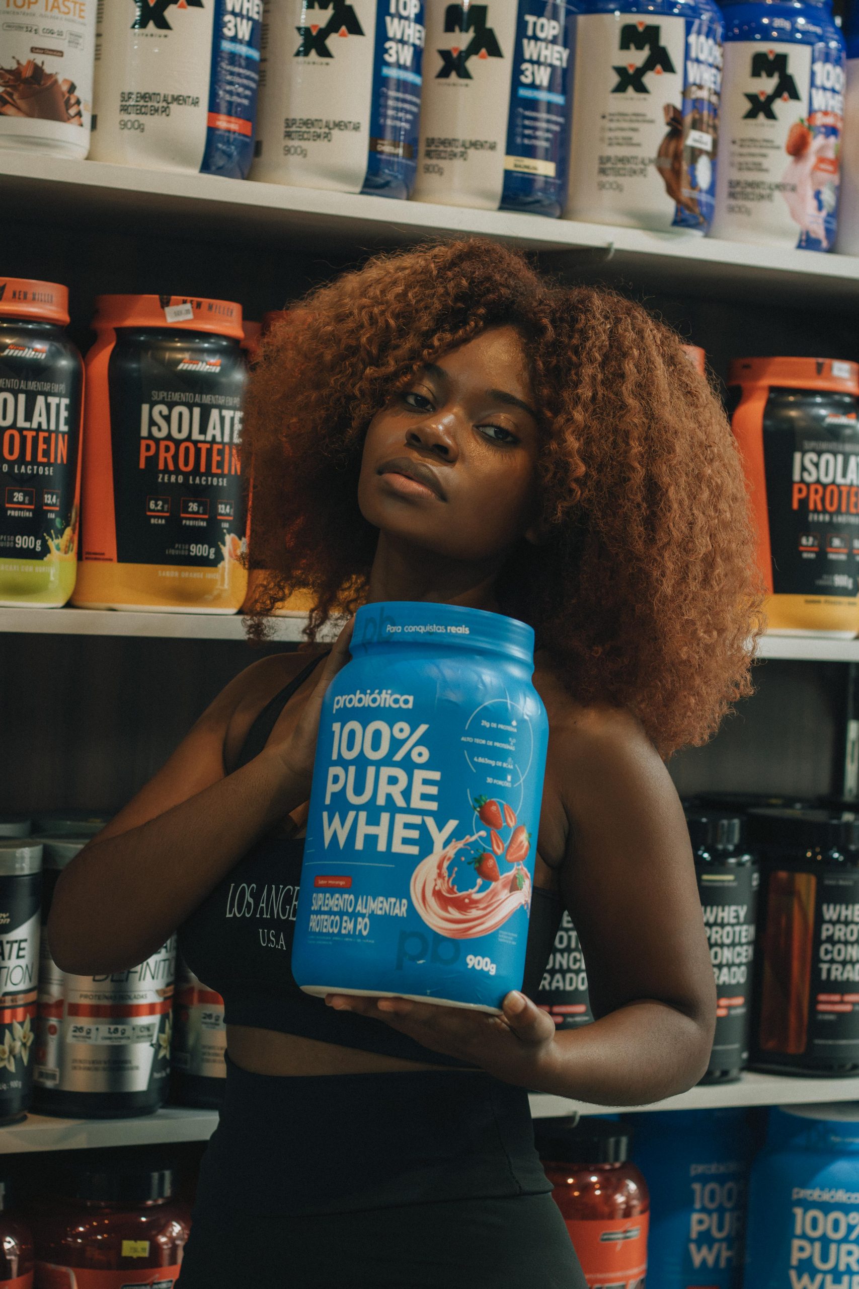 Jeune femme tenant un contenant de protéine de lactosérum 100 % pure dans un magasin de compléments alimentaires.