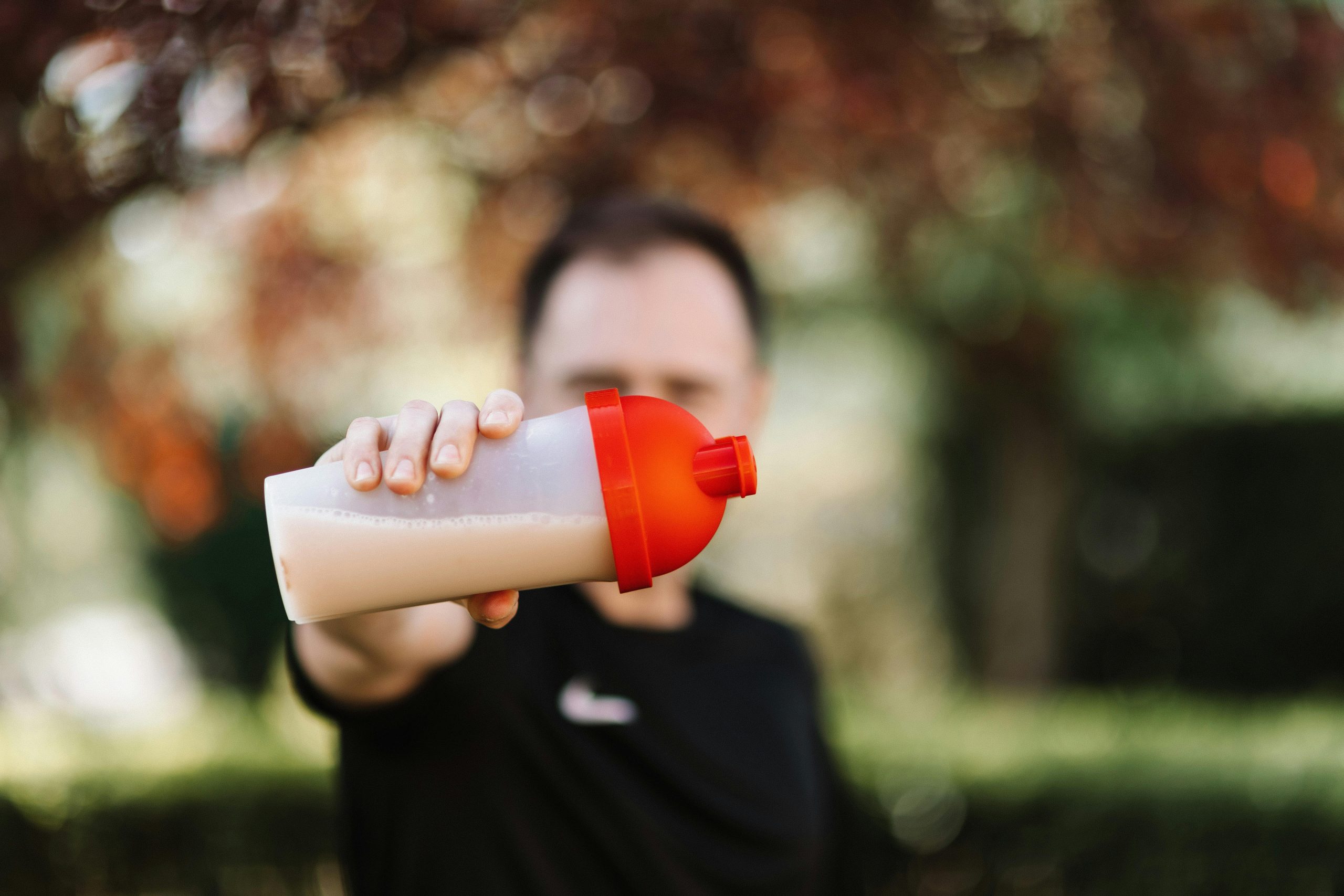 Focus sur un homme tenant un shaker à protéines en plastique en extérieur avec un arrière-plan flou.