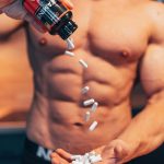 Shirtless man pouring white supplement capsules into his hand with muscles in focus. Homme torse nu versant des capsules de suppléments blanches dans sa main avec les muscles en focus.