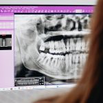 A close-up of a dentist reviewing a dental X-ray image on a computer screen, focusing on oral health analysis. Gros plan d'un dentiste examinant une image de radiographie dentaire sur un écran d'ordinateur, en mettant l'accent sur l'analyse de la santé bucco-dentaire.
