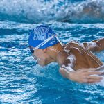 A professional swimmer performing the butterfly stroke in a competitive indoor pool setting with focus on movement. Un nageur professionnel exécutant le papillon dans un bassin intérieur compétitif avec l'accent sur le mouvement.