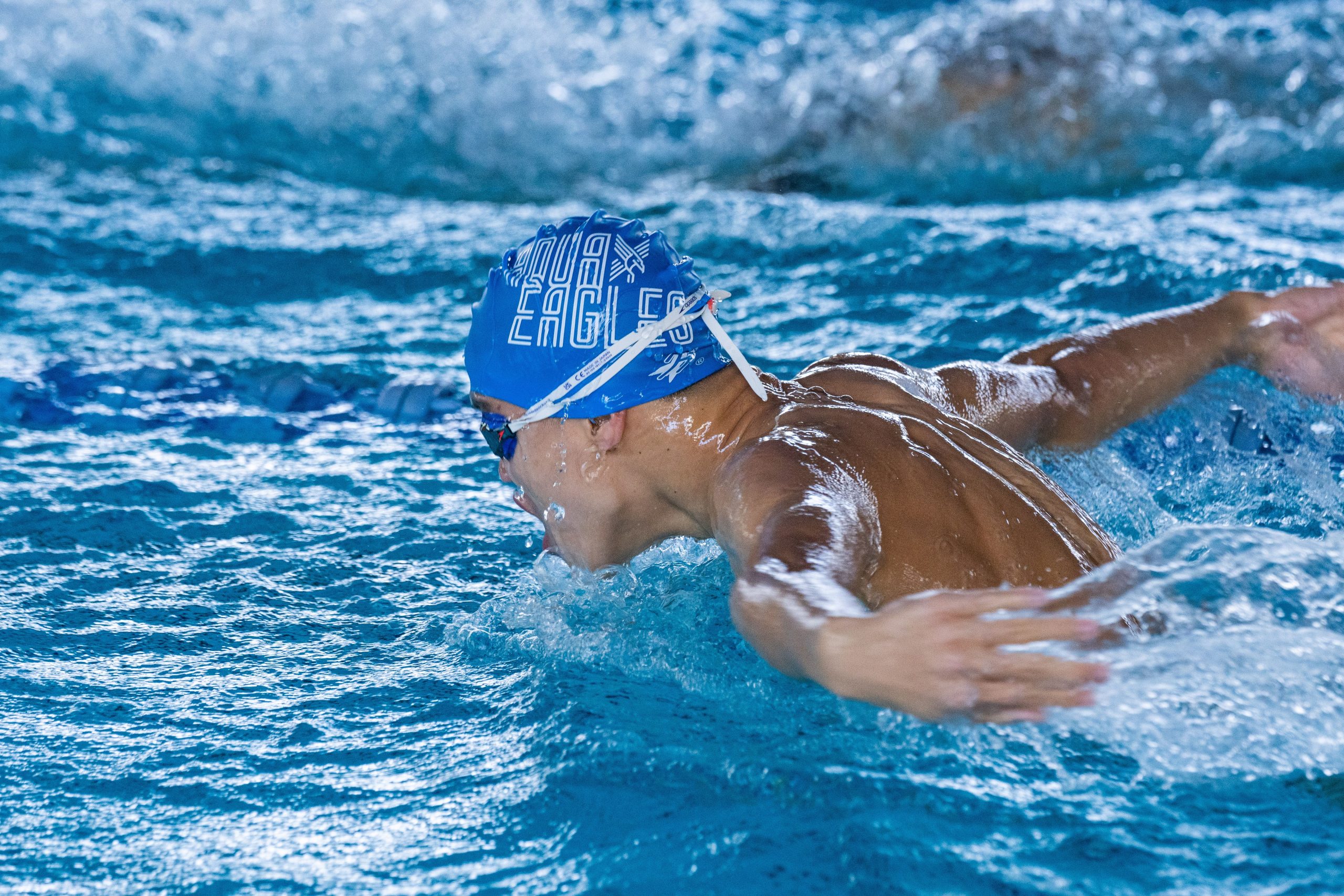 A professional swimmer performing the butterfly stroke in a competitive indoor pool setting with focus on movement. Un nageur professionnel exécutant le papillon dans un bassin intérieur compétitif avec l'accent sur le mouvement.