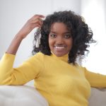 African American woman smiling and holding keys, sitting indoors, symbolizing new home ownership. Femme afro-américaine souriante tenant des clés, assise à l'intérieur, symbolisant l'accession à la propriété d'une nouvelle maison.