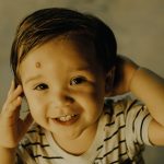 Cute toddler smiling warmly while playing indoors, wearing a striped shirt. Petit enfant souriant chaleureusement en jouant à l'intérieur, portant un chemise rayée.