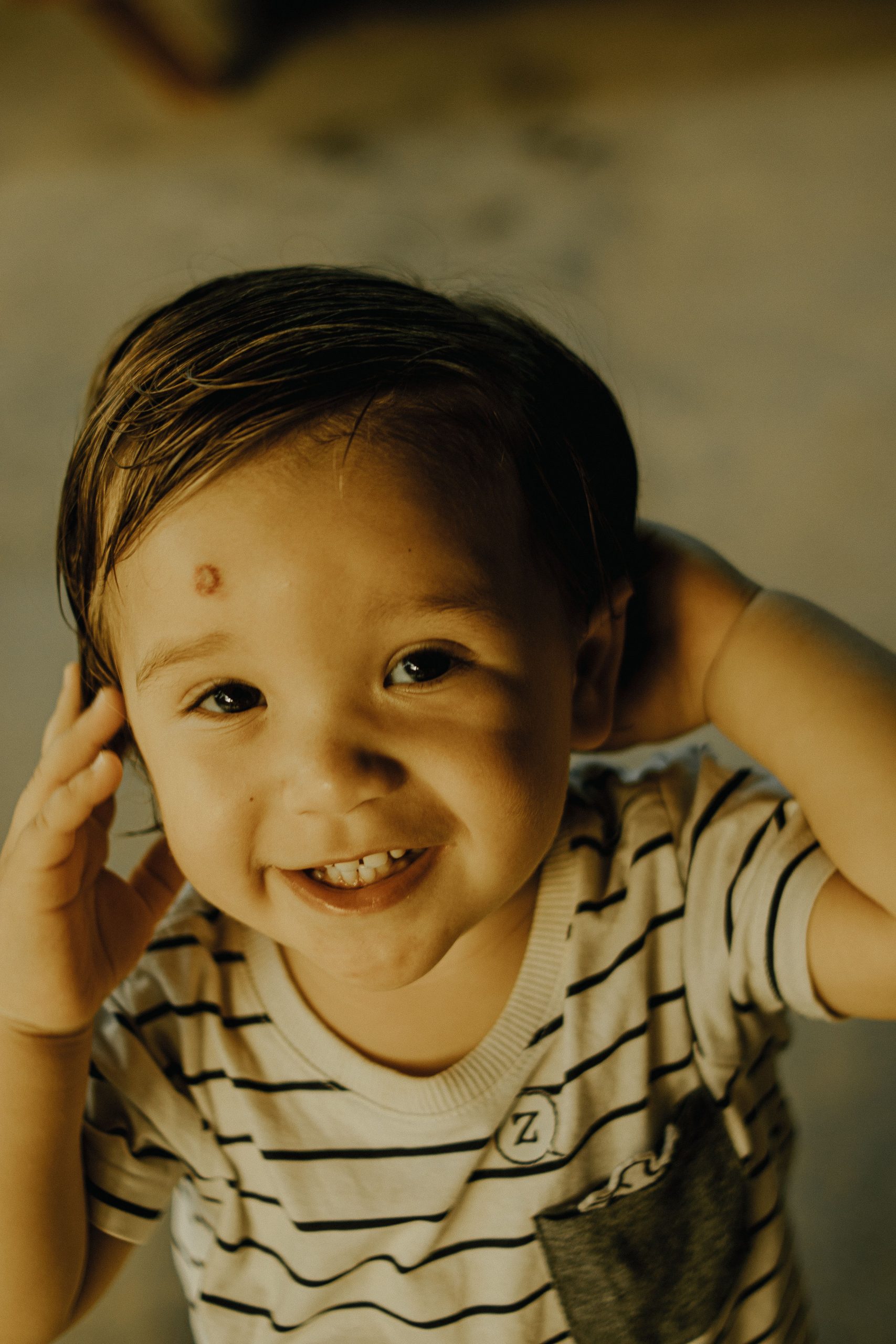 Cute toddler smiling warmly while playing indoors, wearing a striped shirt. Petit enfant souriant chaleureusement en jouant à l'intérieur, portant un chemise rayée.