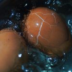 Close-up view of a cracked brown egg boiling in water, showcasing texture and cooking process. Vue rapprochée d'un œuf brun fisssuré bouillant dans l'eau, mettant en évidence la texture et le processus de cuisson.