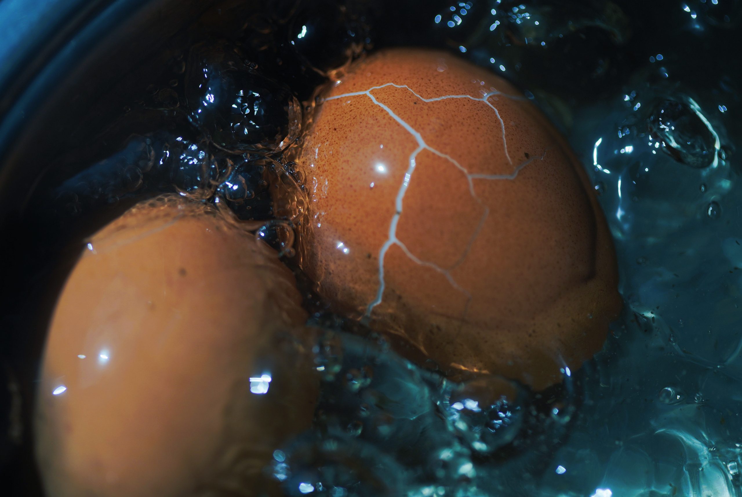 Close-up view of a cracked brown egg boiling in water, showcasing texture and cooking process. Vue rapprochée d'un œuf brun fisssuré bouillant dans l'eau, mettant en évidence la texture et le processus de cuisson.