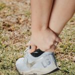 Close-up of a person holding their ankle in a sneaker, indicating pain or injury. Gros plan d'une personne se tenant la cheville dans une basket, indiquant une douleur ou une blessure.