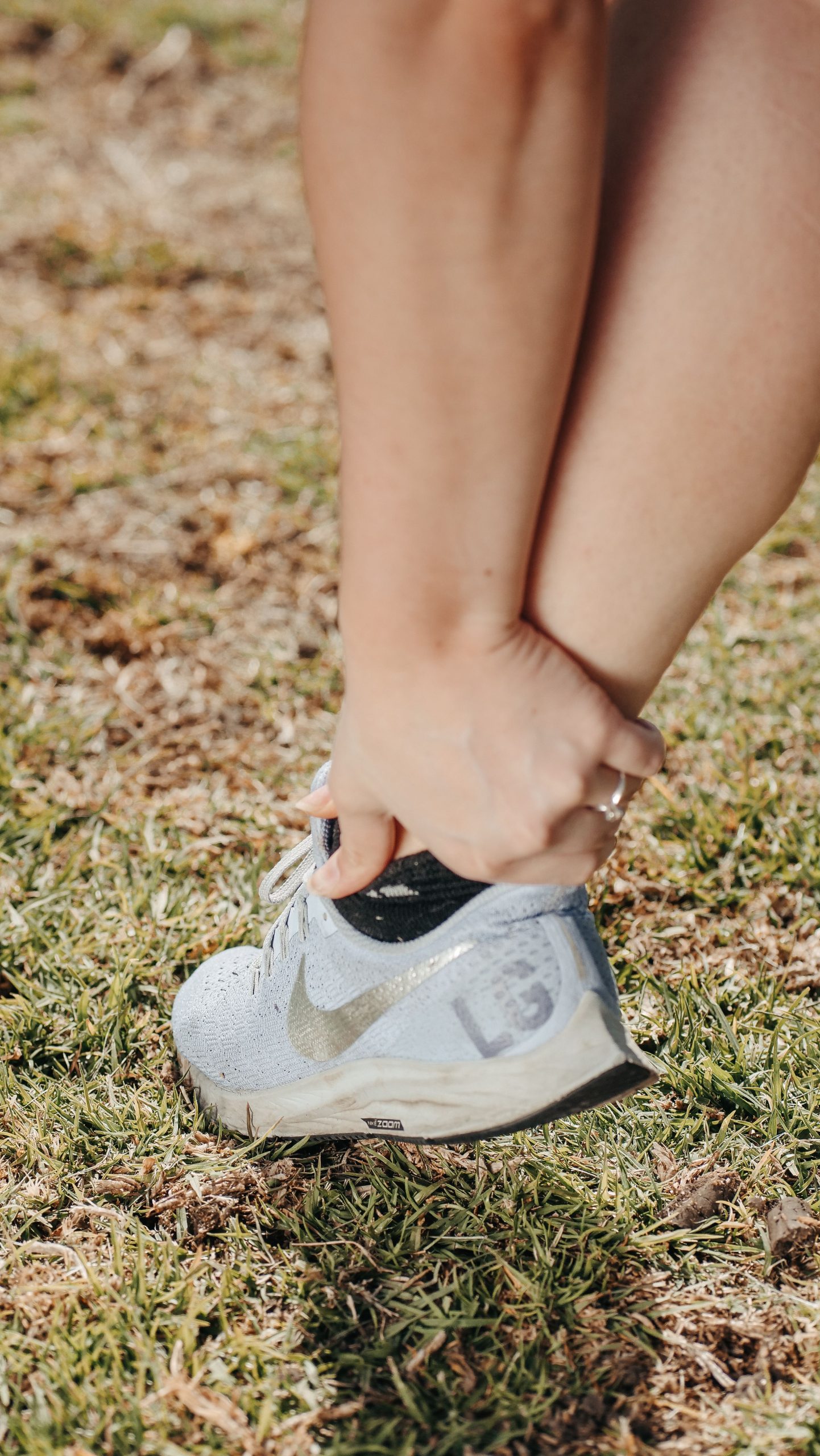 Close-up of a person holding their ankle in a sneaker, indicating pain or injury. Gros plan d'une personne se tenant la cheville dans une basket, indiquant une douleur ou une blessure.