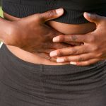 A woman holding her stomach outdoors indicating possible abdominal discomfort or pain. Une femme se tenant le ventre à l'extérieur indiquant un possible inconfort ou une douleur abdominale.