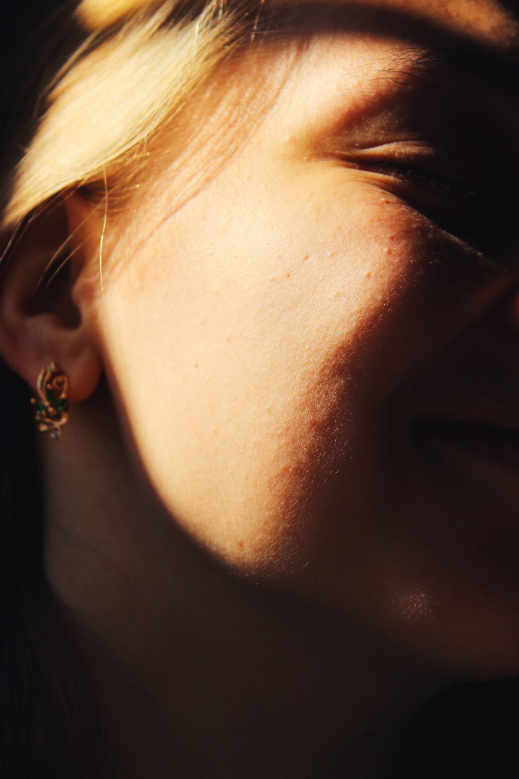 Close-up image capturing a woman smiling with sunlight highlighting her cheek and gold earring. Gros plan capturant une femme souriante avec la lumière du soleil mettant en évidence sa joue et sa boucle d'oreille en or.