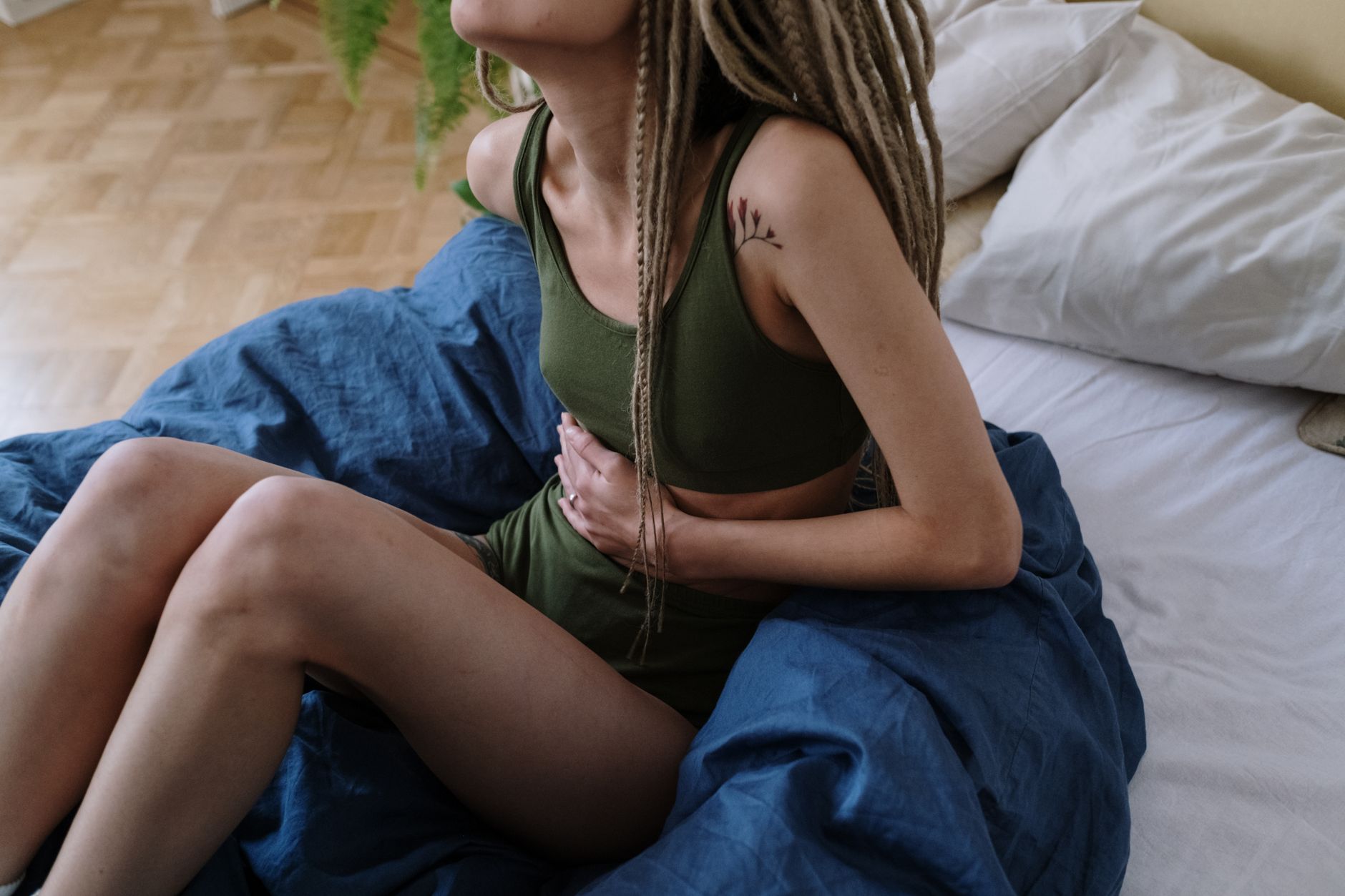 Jeune femme assise sur son lit la main posée sur le ventre