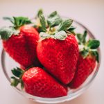 A close-up of bright red strawberries in a clear glass bowl on a soft background. Gros plan de fraises rouges éclatantes dans un bol en verre transparent sur un fond doux.