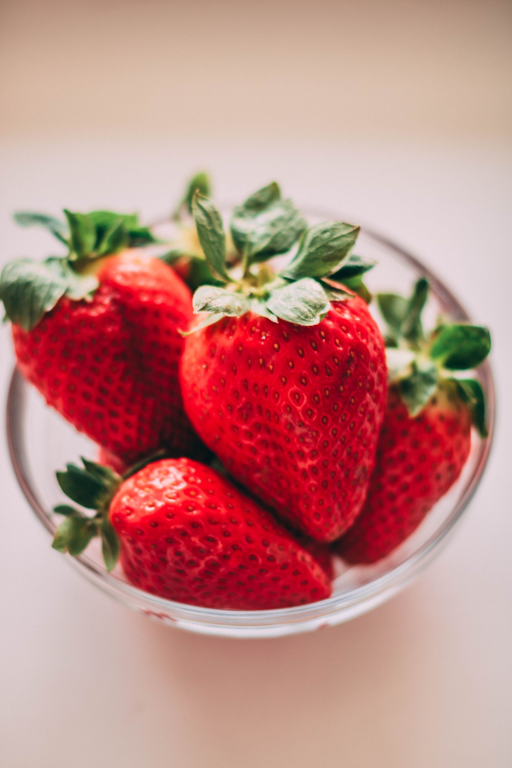 A close-up of bright red strawberries in a clear glass bowl on a soft background. Gros plan de fraises rouges éclatantes dans un bol en verre transparent sur un fond doux.