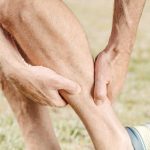 A man outdoors massaging his calf, dealing with muscle pain during sports activities. Un homme en extérieur se massant le mollet, souffrant de douleurs musculaires lors d'activités sportives.