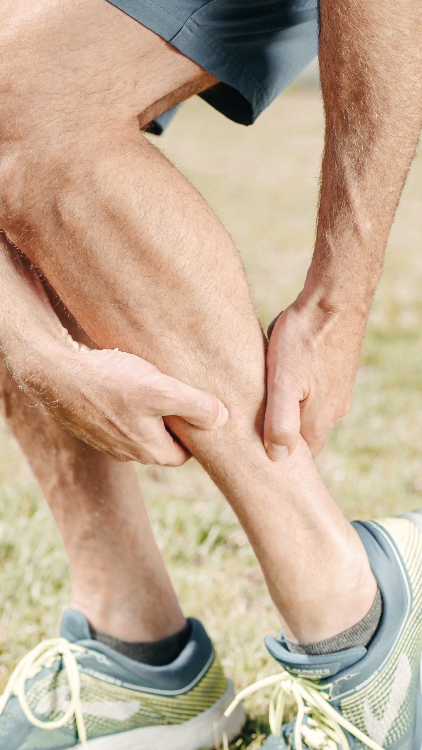 A man outdoors massaging his calf, dealing with muscle pain during sports activities. Un homme en extérieur se massant le mollet, souffrant de douleurs musculaires lors d'activités sportives.