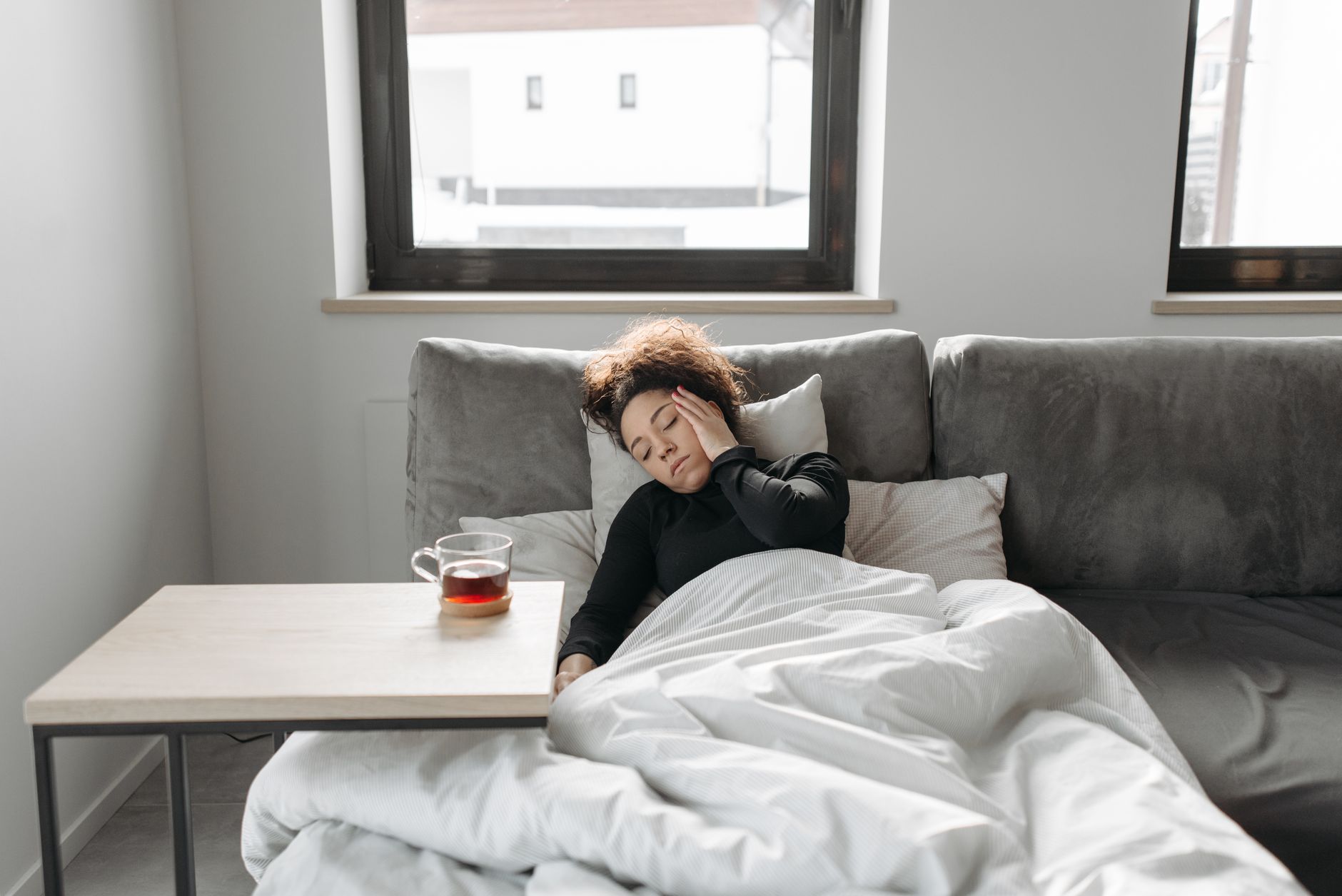 Femme allongée sur un canapé avec une tasse de thé, fatiguée